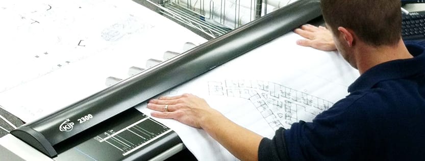 Man feeding a construction document into a large format scanner.