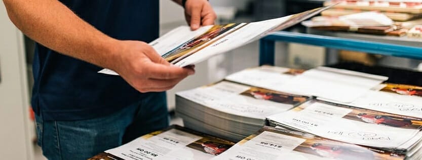 A person holding a sample next to a pile of printed folders.