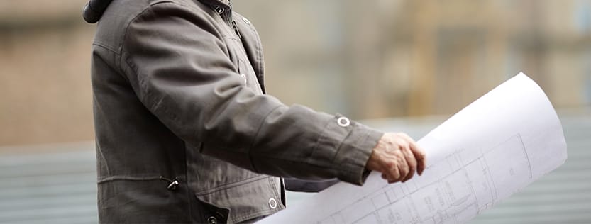A construction worker wearing a coat looking at blueprints outside.