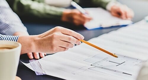 Person holding a pencil and ruler discussing an architectural drawing with someone