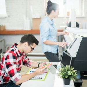 woman operating wide format printer and man looking at pantone color chips