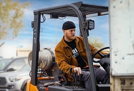 A bearded man loading a truck with a forklift.
