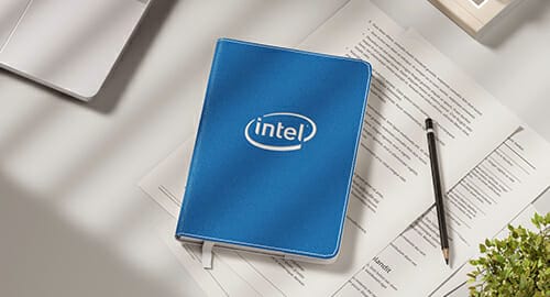 Intel notebook and pencil on top of a desk with papers.