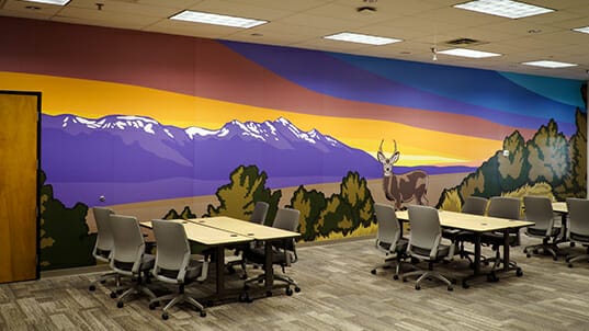 A room with tables and chairs that has one wall covered in full-color artwork.