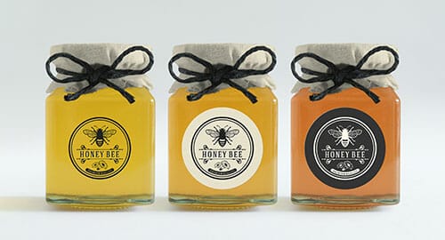 Three honey jars with printing circular labels on them.