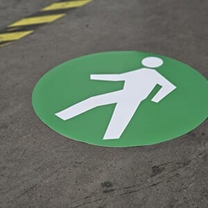 Circular floor decal of a green walkway sign inside a warehouse